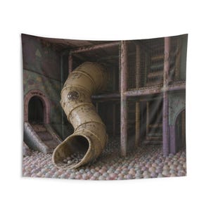 May include: A weathered indoor playground structure featuring a curved yellow tube slide that descends into a large pit filled with numerous small, pale-colored plastic balls. The play area includes metal support frames and arched entryways.