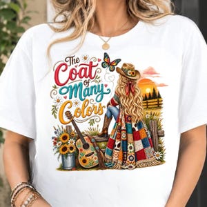 Può includere: Una t-shirt bianca con una stampa grafica di una persona con lunghi capelli biondi che indossa un cappello da cowboy e una coperta patchwork colorata. Il design include una chitarra, girasoli, una farfalla e il testo The Coat of Many Colors.