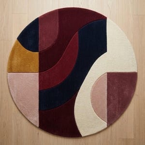 Könnte beinhalten: Ein runder Teppich mit einem getufteten, mehrfarbigen geometrischen Muster. Das Design besteht aus geschwungenen und geraden Segmenten in den Farben Dunkelburgunder, Marineblau, Senfgelb, zartem Rosa und Creme, die eine strukturierte Oberfläche bilden.