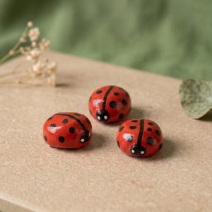 Peut inclure: Trois petites figurines de coccinelles peintes à la main, de forme arrondie. Chaque figurine présente une base rouge vif avec des points noirs distincts, une ligne centrale noire sur le dos et une petite tête noire avec deux points blancs.