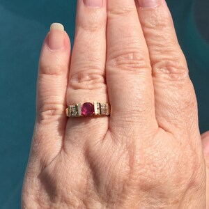 Op de afbeelding: Een gouden ring met een centrale rondgeslepen dieproze edelsteen, geflankeerd door twee rechthoekige, heldere baguette-geslepen stenen aan elke kant, gezet in een kanaalstijl band die het contrast tussen het levendige midden en de stenen benadrukt.