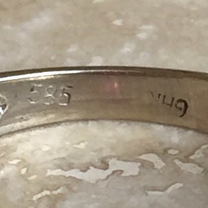 May include: A gold ring band featuring a clear, stamped hallmark on the interior surface. The metal band displays the number 585, which indicates the gold purity, along with an additional partial, partially obscured character mark next to it.