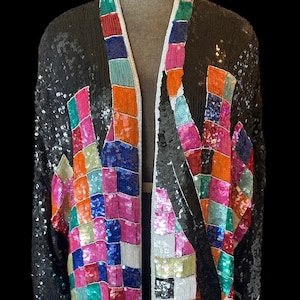 May include: A black sequined kimono with a colorful geometric pattern. The pattern is made up of squares in various shades of pink, blue, green, orange, and white.