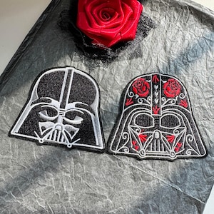 Puede incluir: Dos parches bordados con forma de casco. El parche izquierdo es negro con detalles en blanco y gris. El parche derecho es negro con filigrana blanca, detalles de rosas rojas y formas de corazón rojas. Ambos tienen una barra vertical central.