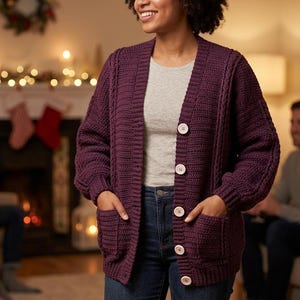 May include: A deep purple, long-sleeved, button-down cardigan featuring a textured crochet knit pattern, a V-neckline, two front patch pockets, and light-colored circular buttons. The garment includes ribbed cuffs and vertical cable knit detailing.