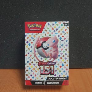 Può includere: Una scatola rettangolare di pacchetti di espansione Pokémon Scarlet & Violet 151 con un personaggio Mew rosa e una grafica Poké Ball. Lo sfondo bianco è coperto da piccole sagome colorate di Pokémon. Il testo sulla scatola recita 151, Booster Bundle e Includes 6 Booster Packs.