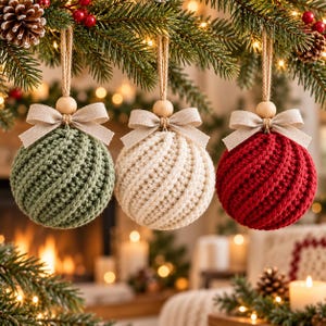 May include: Three spherical crochet ornaments hanging from evergreen branches. Each ornament features a textured, spiralling knit pattern in sage green, cream, and deep red. A natural wooden bead and a beige fabric bow accent the top of each piece.
