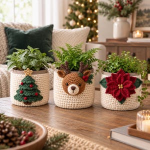 Puede incluir: Tres fundas de ganchillo para macetas en color crema, cada una con un aplique navideño diferente: un árbol de Navidad verde con adornos rojos, una cara de reno marrón con astas y una gran flor de pascua roja con hojas verdes.