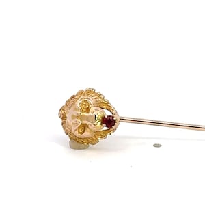 May include: A gold lion head pin with a red stone in its mouth.