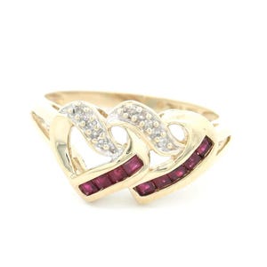May include: A gold ring with two intertwined heart shapes. The hearts are accented with small, clear diamonds and a row of red rubies.