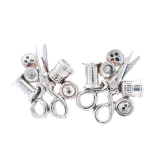 May include: A pair of silver-toned earrings featuring miniature sewing tools. Each earring includes scissors, a thimble, a spool of thread, and buttons. The earrings are designed with a detailed, handcrafted appearance, perfect for a craft enthusiast.