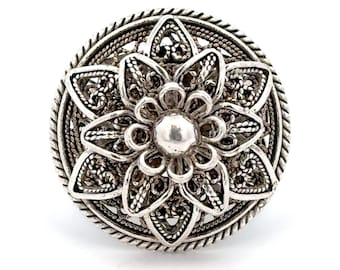 May include: A silver filigree ring with a flower design. The ring is round and has a raised center.