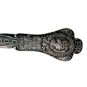 May include: Silver spoon with a detailed design featuring the royal crest of Queen Elizabeth II, the text "H.M. QUEEN ELIZABETH II 1953" and the text "ER OIT QUI-MAL-Y PENSE"