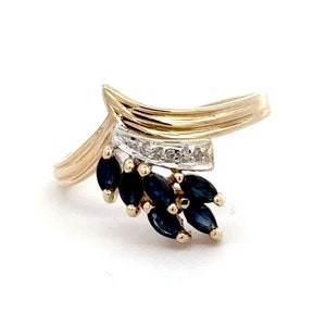 May include: A gold ring with a delicate design featuring a cluster of blue sapphires and a row of small diamonds.