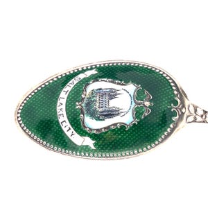 May include: A vintage silver spoon with a green enamel bowl. The bowl features a white banner with "SALT LAKE CITY" and a detailed illustration of a building. The spoon has a decorative handle.