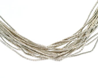 May include: Silver-toned necklace composed of numerous thin, rectangular beads. The beads are strung together, creating a layered effect. The necklace is set against a white background, highlighting its metallic sheen and intricate design.
