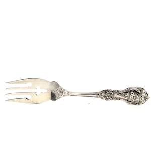 May include: Silver serving fork with three tines and a decorative handle. The fork features an ornate floral design on the handle and a cut-out cross shape near the tines. The utensil is made of a shiny, reflective metal.