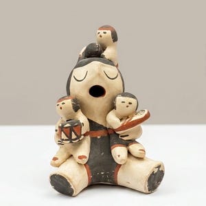 May include: A hand-painted ceramic storyteller figurine featuring a large central figure with eyes closed and mouth open, surrounded by three smaller figures. The piece is decorated in cream, black, and terracotta red paint with geometric patterns.