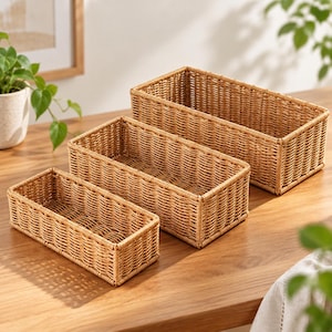 May include: A set of three rectangular storage baskets with a woven light brown finish. The baskets are arranged in a cascading formation, featuring an open-top design with a consistent grid-like pattern throughout the sides and base.