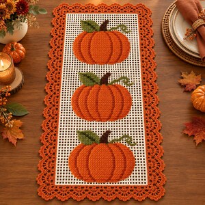 Peut inclure: Un chemin de table rectangulaire avec une base à motif de grille blanche et trois citrouilles orange crochetées, chacune avec une feuille verte et une tige brune. Le chemin est bordé d'une bordure en dentelle orange crochetée.