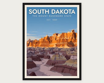 Puede incluir: Un póster enmarcado que muestra un paisaje de Dakota del Sur con formaciones rocosas naranjas bajo un cielo azul. El texto dice SOUTH DAKOTA, THE MOUNT RUSHMORE STATE, EST. 1889. La escena representa un terreno geológico estratificado en tonos marrones y morados.