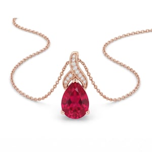 May include: A rose gold necklace featuring a pear-shaped red gemstone pendant. The pendant is accented with a curved, textured bail set with small white diamonds. The chain is a delicate cable link style, matching the rose gold metal tone.