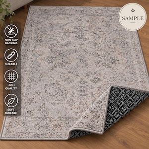 K&ouml;nnte beinhalten: Ein rechteckiger Teppich mit einem hellgrauen und beigen Blumenmuster und einer dekorativen Bord&uuml;re. Der Teppich ist an einer Ecke umgeschlagen und zeigt eine schwarze, rutschfeste Unterseite mit wei&szlig;en Punkten. Der Text SAMPLE ist zu sehen.