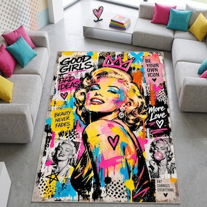Könnte beinhalten: Ein rechteckiger Teppich mit einem lebendigen Pop-Art-Porträt einer blonden Frau mit einer rosa Krone. Das Design umfasst Graffiti-Farbspritzer, schwarz-weiße Muster und den Text Good Girls, Bad Ideas, Be Your Own Icon sowie Beauty Never Fades.