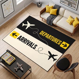 Könnte beinhalten: Ein rechteckiger Teppich mit geteiltem Design, bestehend aus einem schwarzen Bereich mit der Aufschrift DEPARTURES und einem cremefarbenen Bereich mit der Aufschrift ARRIVALS. Er zeigt zwei Flugzeugsilhouetten, Flugbahnen, gelbe Pfeile und Text.