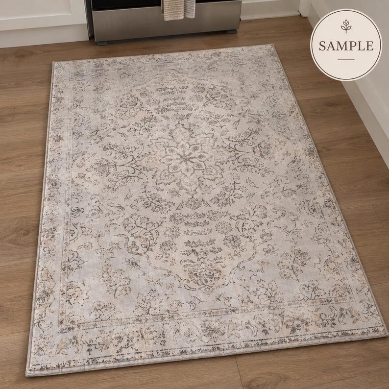 K&ouml;nnte beinhalten: Ein rechteckiger Teppich mit einem verblassten, abgenutzten Muster in den Farben Hellgrau, Beige und Creme. Das Design umfasst ein zentrales Blumenmedaillon, das von komplizierten botanischen Motiven und einem dekorativen Rahmen umgeben ist.