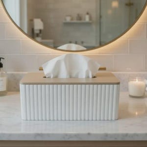 May include: A rectangular tissue box holder featuring a white, vertically ribbed exterior body and a smooth, light-toned wooden lid. A single white facial tissue is pulled through the central rectangular opening on the top of the container.