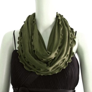 May include: A green infinity scarf with a ruffled edge. The scarf is made of a soft, stretchy fabric and is perfect for adding a touch of color to any outfit.