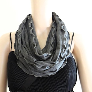 May include: A gray infinity scarf with a ruffled edge. The scarf is made of a soft, stretchy fabric and is perfect for adding a touch of warmth and style to any outfit.