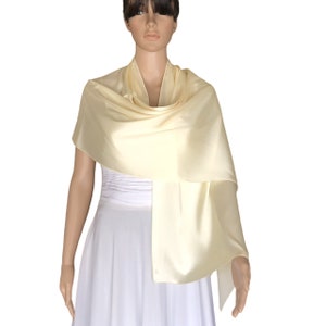 May include: A pale yellow satin shawl draped over a white dress. The shawl is soft and flowing, and would be a beautiful addition to any formal outfit.