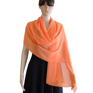 May include: A bright orange chiffon scarf draped over a model's shoulders. The scarf is lightweight and sheer, making it perfect for adding a touch of color to any outfit.