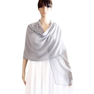 May include: A light grey shawl made of a soft, drapey fabric. The shawl is draped around the shoulders of a person wearing a white dress.