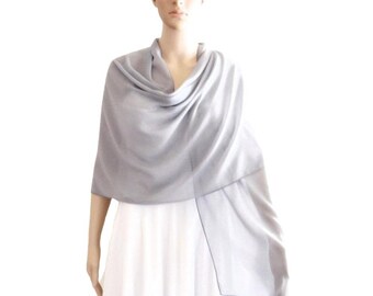 May include: A light gray shawl made of a soft, drapey fabric. The shawl is draped around the shoulders of a person wearing a white dress.