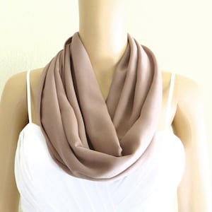 May include: A soft, brown infinity scarf made of a lightweight fabric. The scarf is draped around a mannequin's neck.