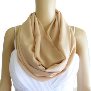 May include: A light beige infinity scarf made of soft fabric. The scarf is draped around a mannequin's neck.