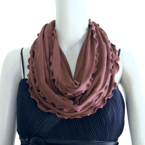 Op de afbeelding: Een bruine oneindige sjaal met een gerimpelde rand. De sjaal is gemaakt van een zachte, rekbare stof en is perfect om elke outfit een vleugje warmte en stijl te geven.