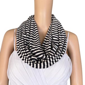 May include: A black and white striped infinity scarf made of soft fabric. The scarf is worn around the neck of a mannequin.