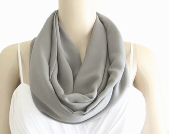 May include: A gray infinity scarf made of soft fabric. The scarf is folded in a loop and draped around a mannequin's neck.