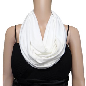 May include: A white infinity scarf made of soft fabric. The scarf is worn around the neck and drapes down the front of the chest.