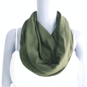 May include: A soft, olive green infinity scarf made of a stretchy fabric. The scarf is worn around the neck and drapes down the chest.