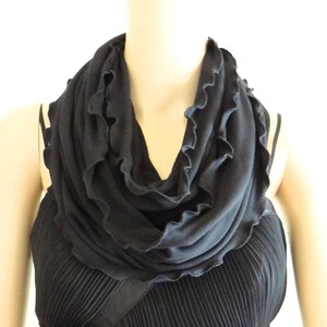 May include: A black infinity scarf with a ruffled edge. The scarf is made of a soft, stretchy fabric and is perfect for adding a touch of style to any outfit.