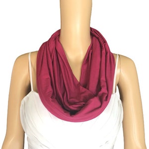May include: A close-up of a maroon infinity scarf made of soft fabric. The scarf is worn around the neck of a mannequin.