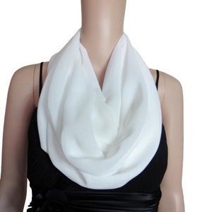 May include: A white, soft, and lightweight infinity scarf made of chiffon fabric. The scarf is draped around a mannequin's neck, showcasing its versatility and draping capabilities.