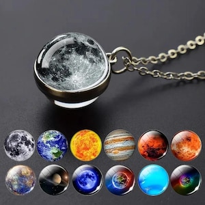 May include: A silver-toned necklace featuring a round glass pendant with a detailed lunar surface image. Below the pendant are twelve additional circular glass cabochons displaying various celestial bodies, including planets and moons in vibrant colours.