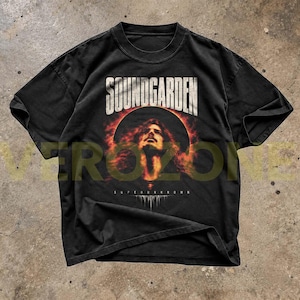 May include: A black short-sleeve t-shirt featuring a graphic print of the band Soundgarden. The design includes the text SOUNDGARDEN at the top, a central portrait of a person surrounded by a fiery orange sun, and the word SUPERUNKNOWN at the bottom.