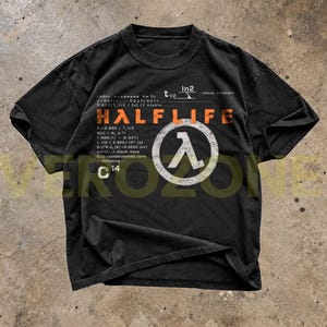 Puede incluir: Una camiseta negra de manga corta con un estampado gráfico que incluye el texto naranja HALFLIFE, un símbolo lambda blanco dentro de un círculo y varias fórmulas científicas, incluyendo ecuaciones de constante de desintegración y C14.